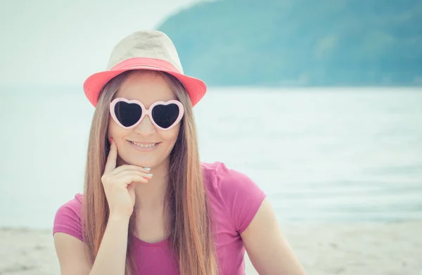 Mujer feliz turista en sombrero de paja y gafas de sol sentado en la playa, tiempo libre en la playa — Foto de Stock