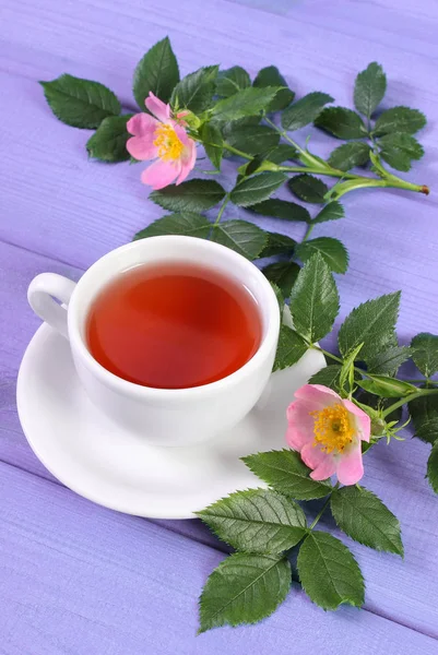 Tasse Tee und Wildrosenblume auf violetten Brettern — Stockfoto