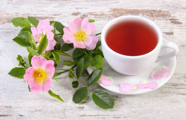Tasse Tee und Wildrosenblume auf altem rustikalem Holzgrund — Stockfoto