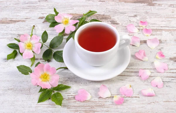 Tasse Tee und Wildrosenblume auf altem rustikalem Holzgrund — Stockfoto