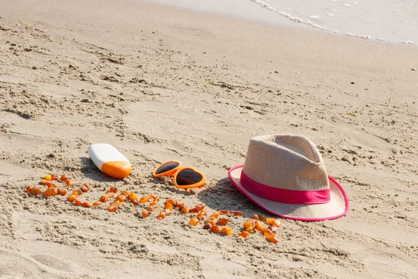 Palabra de verano, gafas de sol, loción solar y sombrero de paja en la arena en la playa, hora de verano — Foto de Stock