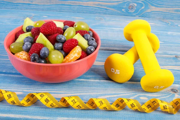 Fresh fruit salad and centimeter with dumbbells, healthy lifestyle and nutrition concept