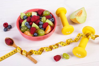 Taze meyve salatası ve santimetre dambıl, sağlıklı yaşam ve beslenme kavramı ile