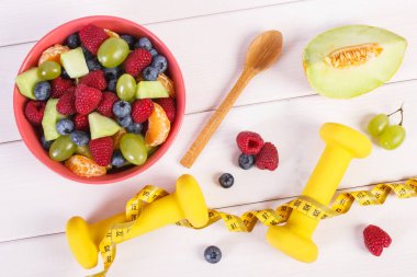 Taze meyve salatası ve santimetre dambıl, sağlıklı yaşam ve beslenme kavramı ile