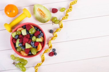 Taze meyve salatası ve santimetre dambıl, sağlıklı yaşam ve beslenme kavramı ile