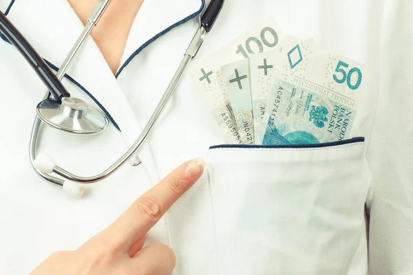 Vrouw arts met de stethoscoop Pools munt geld in de zak van de schort tonen — Stockfoto