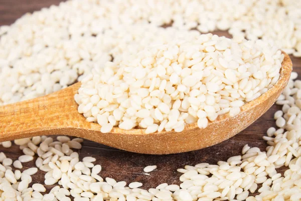 Sesame seeds with wooden spoon on board — Stock Photo, Image