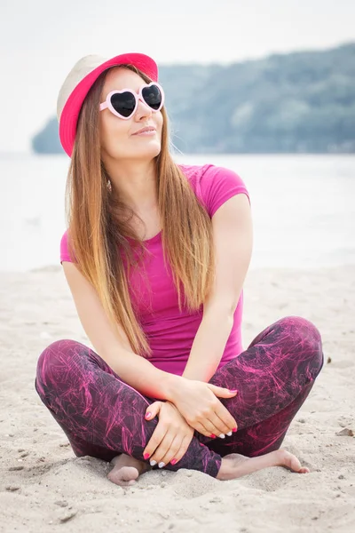 Mujer feliz turista en sombrero de paja y gafas de sol sentado en la playa, tiempo libre en la playa — Foto de Stock