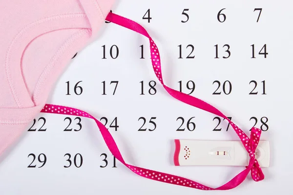 Test di gravidanza con risultato positivo nastro avvolto e body per neonato sul calendario — Foto Stock