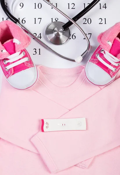 Test di gravidanza con esito positivo, abbigliamento per neonato e stetoscopio sul calendario — Foto Stock