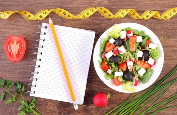 Fresh prepared greek salad with vegetables, tape measure and notepad for writing notes, healthy nutrition and slimming concept — Stock Photo, Image