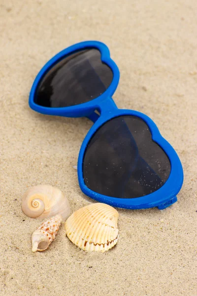 在心和海滩上的沙子贝壳形状的蓝色太阳镜 — 图库照片