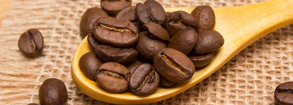 Куча кофейных зерен с деревянной ложкой на холсте джута — стоковое фото