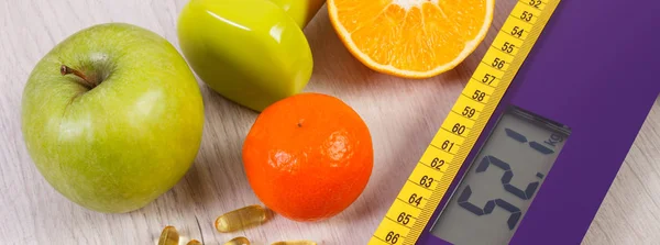 Digital scale with tape measure, dumbbells, tablets, fruits, slimming concept — Stock Photo, Image