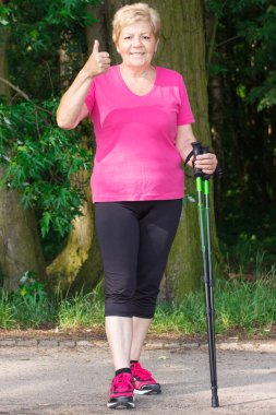 Yaşlı kadın kıdemli Nordik yürüyüş ve başparmak yukarıya, sportif yaşam gösterilen pratik