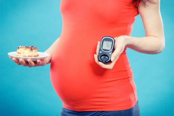 Вагітна жінка тримає лічильник глюкози з хорошим рівнем цукру і шматочком чізкейку, діабетом і харчуванням під час вагітності — стокове фото