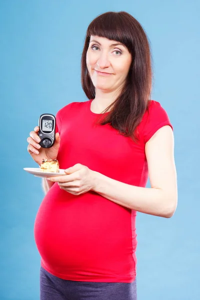 Femme enceinte tenant un glucomètre avec un taux de sucre et un morceau de gâteau au fromage, le diabète et la nutrition pendant la grossesse — Photo