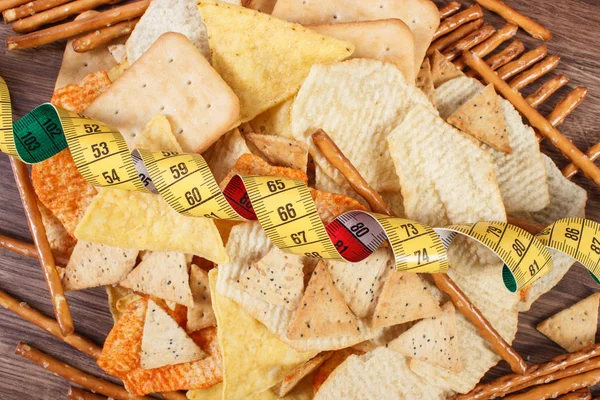 Centimeter with salted potato crisps, cookies and breadsticks, unhealthy food and slimming concept — Stock Photo, Image
