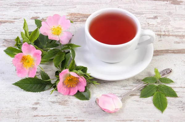 Tasse heißen Tee und Wildrosenblume auf rustikalem Holzgrund — Stockfoto