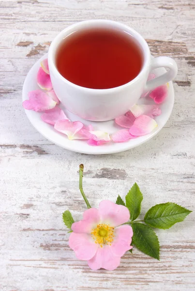 Kopje warme thee en wild rose bloem op rustieke houten achtergrond — Stockfoto