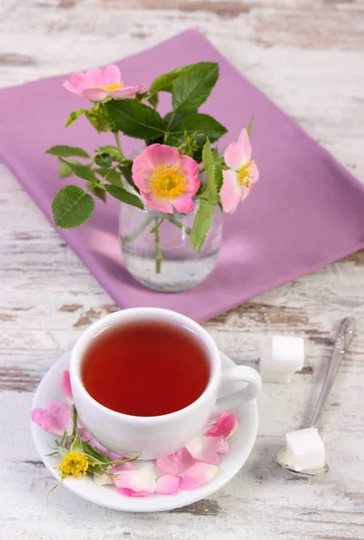 Xícara de chá e rosa selvagem flor no fundo de madeira rústica — Fotografia de Stock