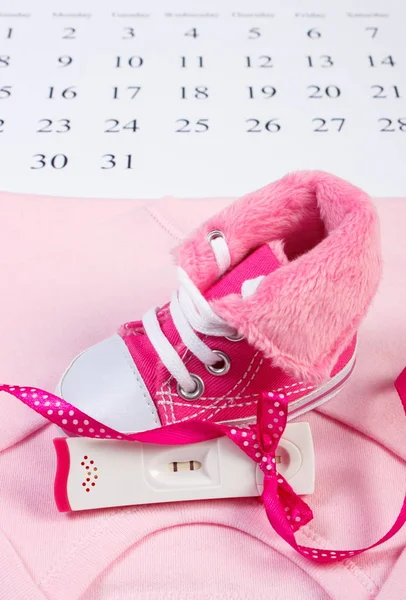 Test di gravidanza con risultato positivo e abbigliamento per il neonato sdraiato sul calendario, in attesa per il bambino — Foto Stock