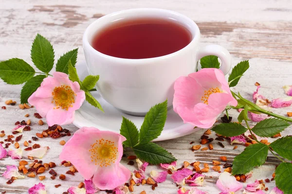 Tasse heißer Tee mit Wildrosenblume auf alten rustikalen Planken — Stockfoto