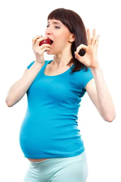 Счастливая беременная женщина ест свежее яблоко и показывает знак ОК, здоровая пища во время беременности — стоковое фото