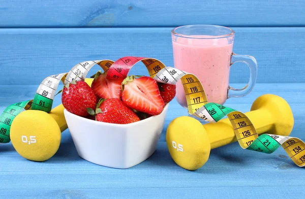 Fresh strawberries, milkshake, dumbbells and centimeter on blue boards, concept of healthy and sporty lifestyle — Stock Photo, Image