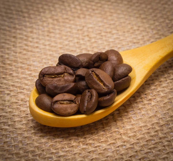 Haufen Kaffeekörner mit Holzlöffel auf Jute — Stockfoto