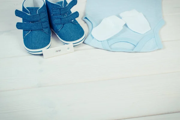 Foto vintage, prueba de embarazo con resultado positivo y ropa para recién nacidos, concepto de espera para el bebé —  Fotos de Stock