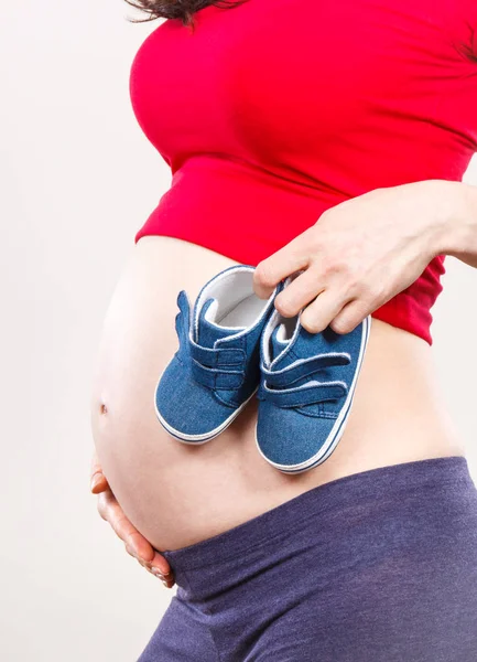 Беременная женщина в детской обуви, концепция ожидания ребенка — стоковое фото