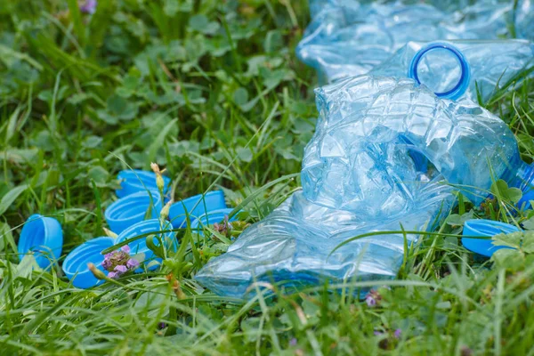 Garrafas de plástico e tampas de garrafa na grama verde no parque, conceito de lixo do meio ambiente — Fotografia de Stock
