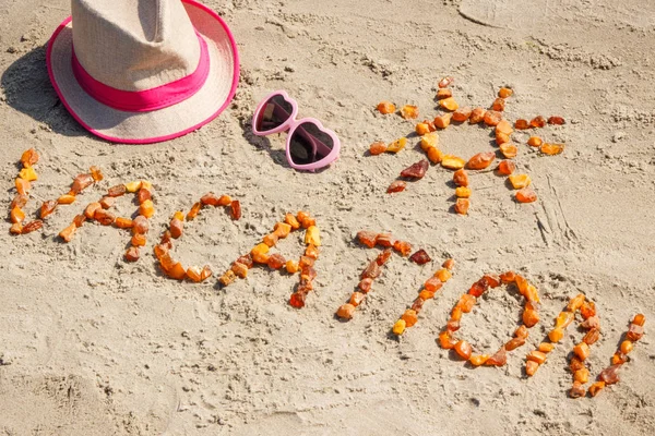 Word vacation with shape of sun, sunglasses and straw hat at beach — Stock Photo, Image