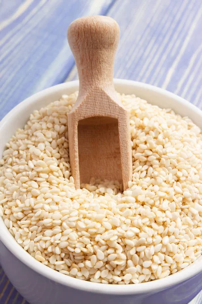 Sesame seeds with wooden scoop in bowl on purple boards — Stock Photo, Image