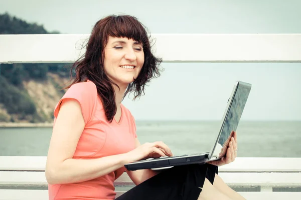 Винтажное фото, женщина сидит на скамейке у моря со своим ноутбуком, используя компьютерную концепцию — стоковое фото