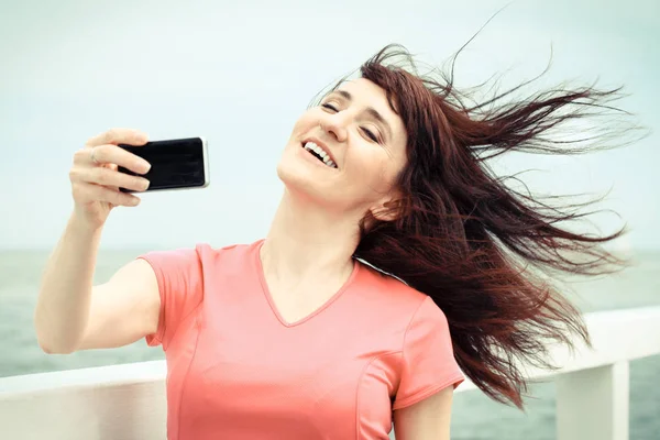 Женщина делает селфи фото со смартфоном на пляже на берегу моря, используя концепцию мобильного телефона — стоковое фото