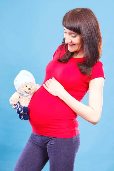 Felice donna incinta sorridente in possesso di peluche orsacchiotto al ventre, concetto di giocattolo per bambini — Foto Stock