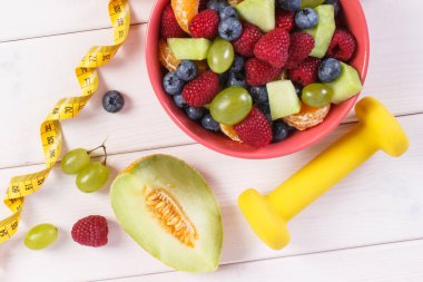 Taze meyve salatası ve şerit metre ile halter, sağlıklı yaşam gıda ve beslenme kavramı