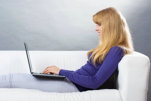 Счастливая улыбающаяся женщина с ноутбуком, сидящая на диване, современными технологиями и интернет-концепцией серфинга — стоковое фото