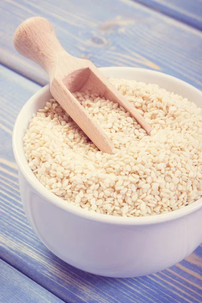 Semillas de sésamo con cuchara de madera en cuenco de vidrio blanco en tablas — Foto de Stock