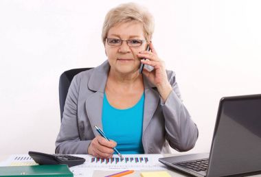 Smartphone üzerinde konuşmak ve ofis masasında çalışan yaşlı bir iş kadını