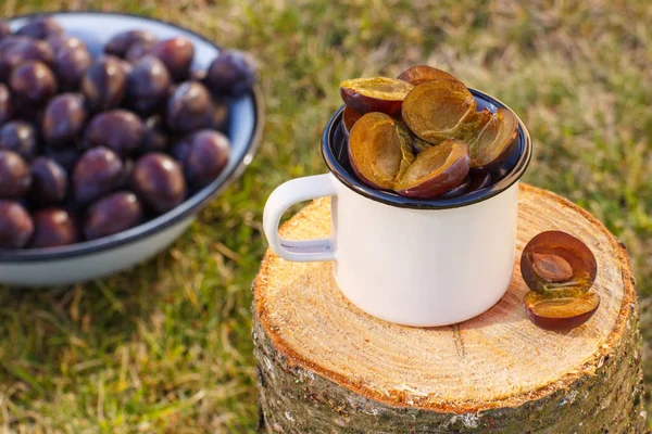 Ameixas em caneca metálica no toco de madeira no jardim no dia ensolarado — Fotografia de Stock