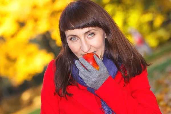 Smiling woman eating fresh apple in autumn park — Stock Photo, Image