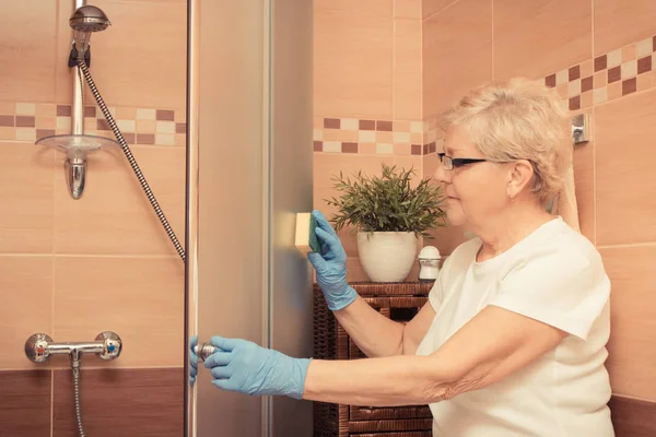 Старшая женщина с губкой и уборка душ, домашние обязанности концепции — стоковое фото
