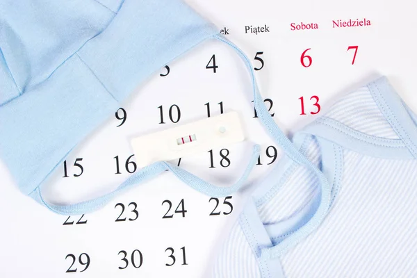 Test di gravidanza con risultato di gravidanza e abbigliamento per neonato sul calendario, in attesa per il bambino — Foto Stock
