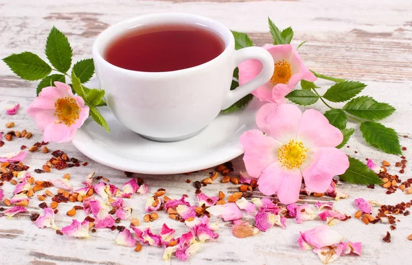 喝杯热茶与旧仿古木制板上的野生玫瑰花朵 — 图库照片