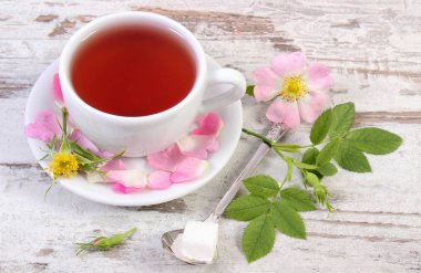 Fincan çay ve eski rustik tahta üzerinde yabani gül çiçek