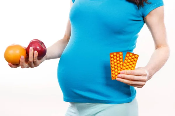 Zwangere vrouw houden van verse rijpe vruchten en medische pillen of supplementen, keuze tussen gezonde voeding en pillen — Stockfoto