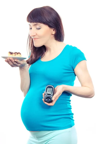 Беременная женщина с чизкейком и глюкозой в руках с результатом уровня сахара, диабета во время беременности — стоковое фото